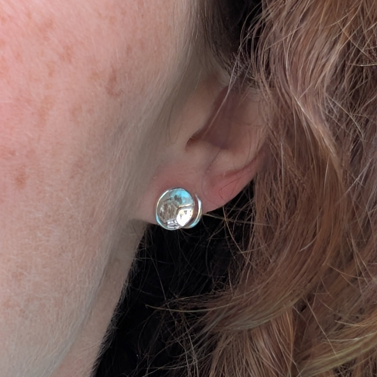 Silver honeycomb disc stud earrings shown being worn, showing the size of the round patterned silver stud against the ear.