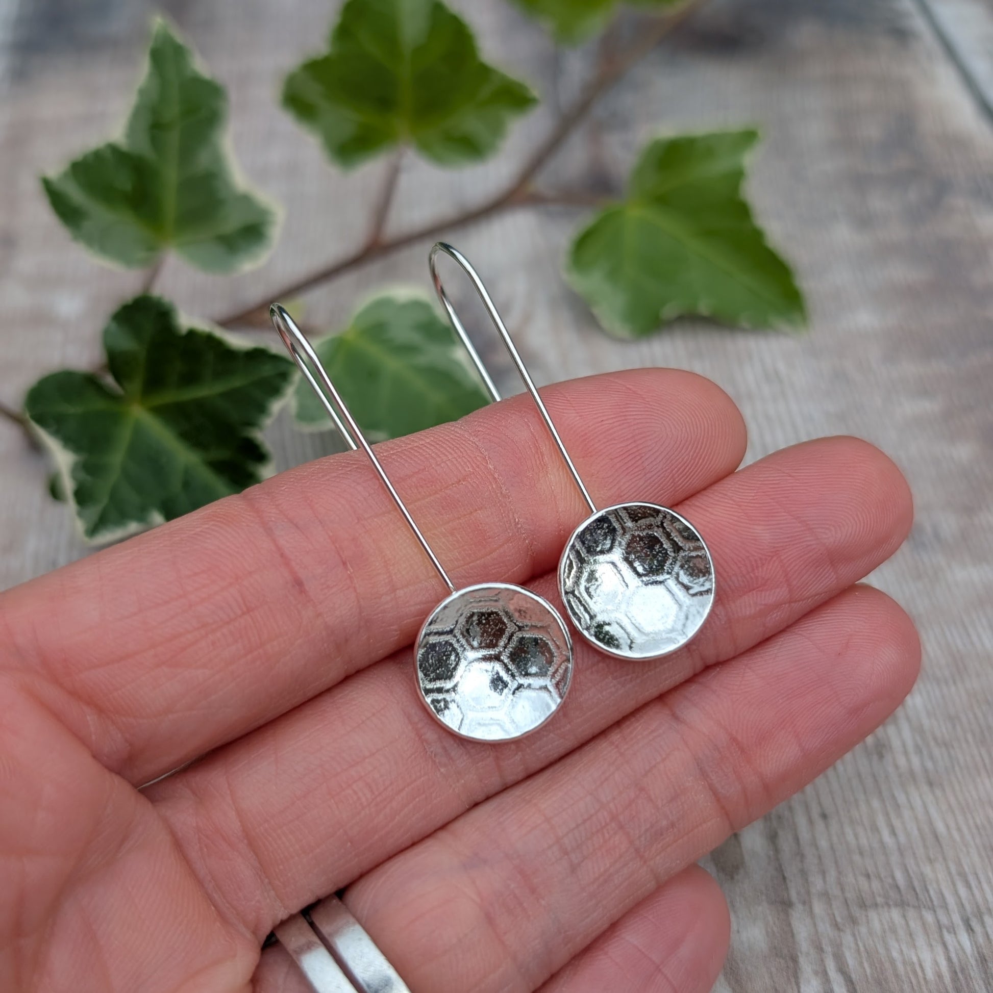 Silver honeycomb long disc earrings handmade from recycled Sterling Silver, held in a hand to show their size and honeycomb texture.