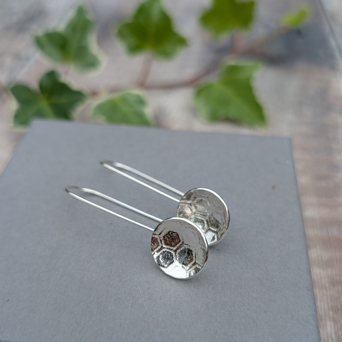 Silver honeycomb long disc earrings displayed on a grey background, showing the honeycomb pattern added to the silver.