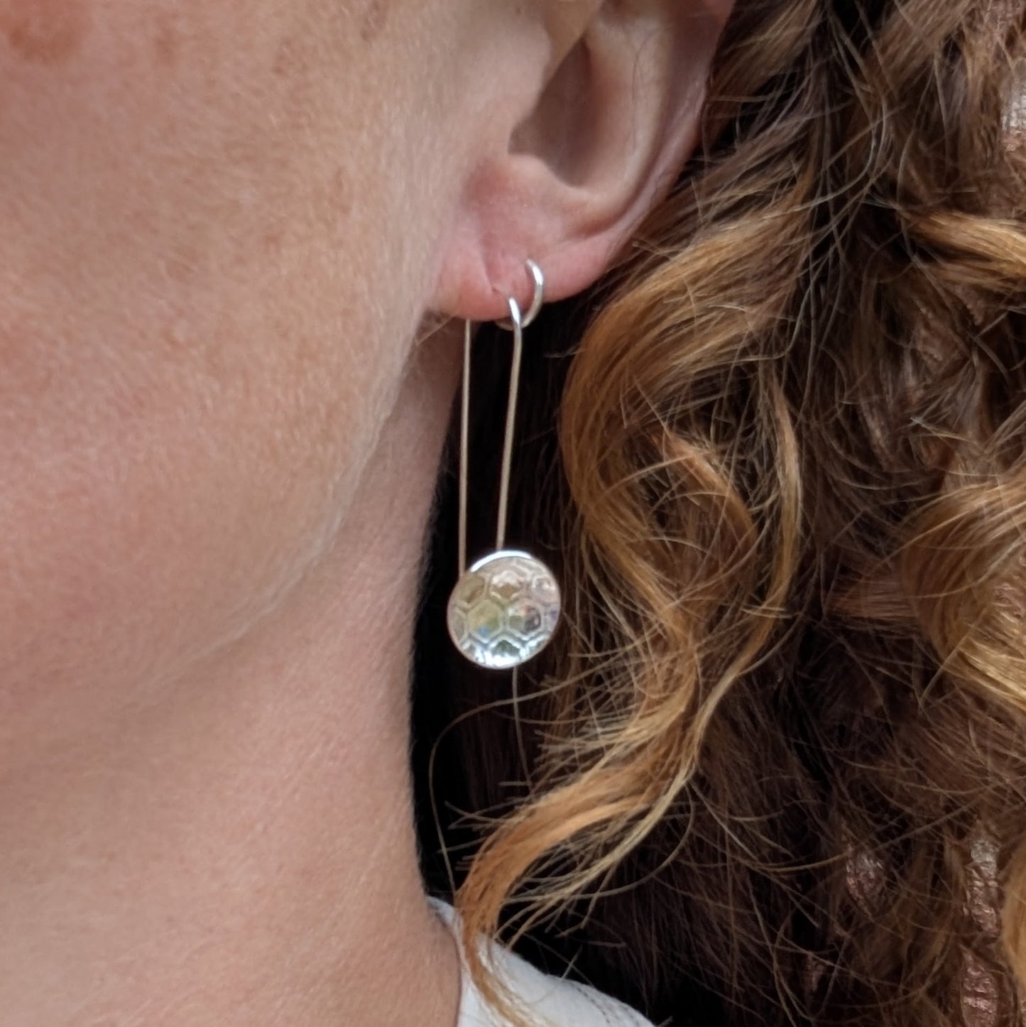 Silver honeycomb long disc earrings being worn, showing the long drop design and textured round silver discs.