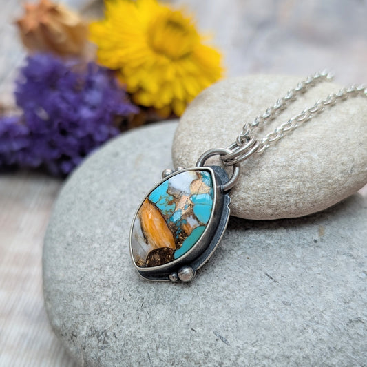 Close-up of the Silver Kingman Turquoise Necklace resting on stacked pebbles, highlighting the intricate pattern within the stone and oxidised silver detailing.