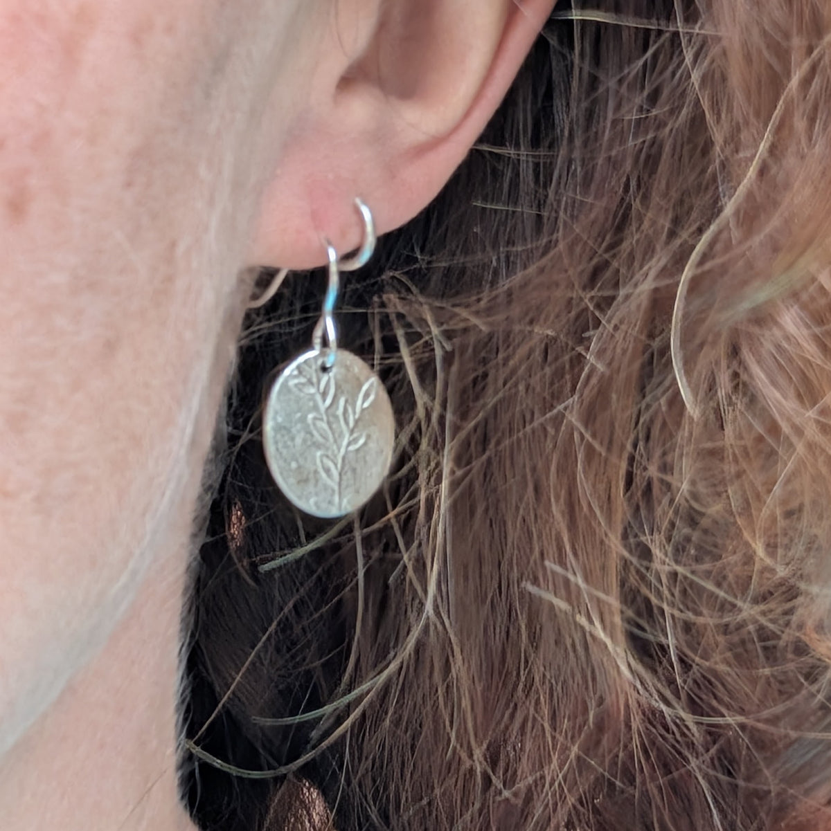 Silver leafy vine oval disc earrings being worn, showing the size and drop of the patterned silver discs.