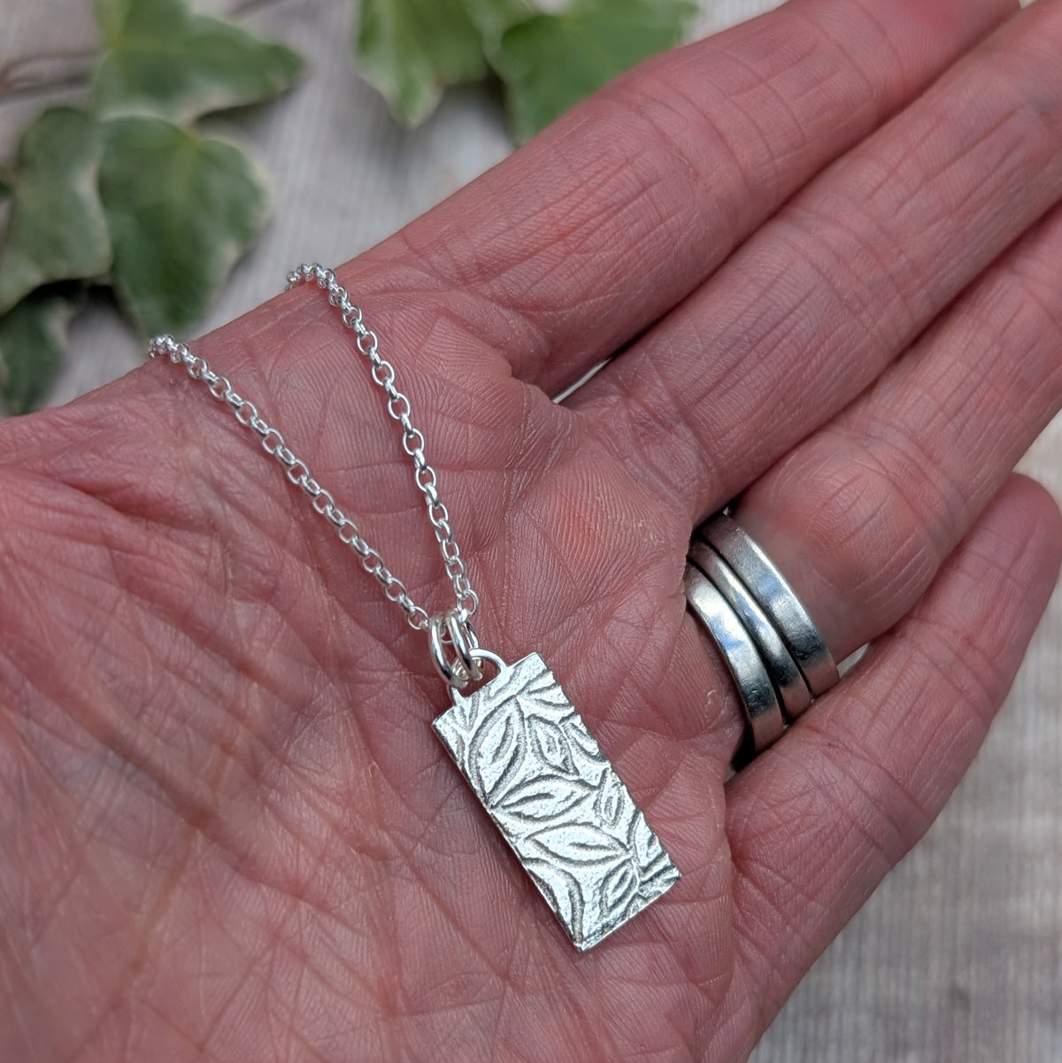 Silver leaves rectangle necklace handmade from recycled Sterling Silver, shown resting in a hand to show the size and detailed leafy pattern.
