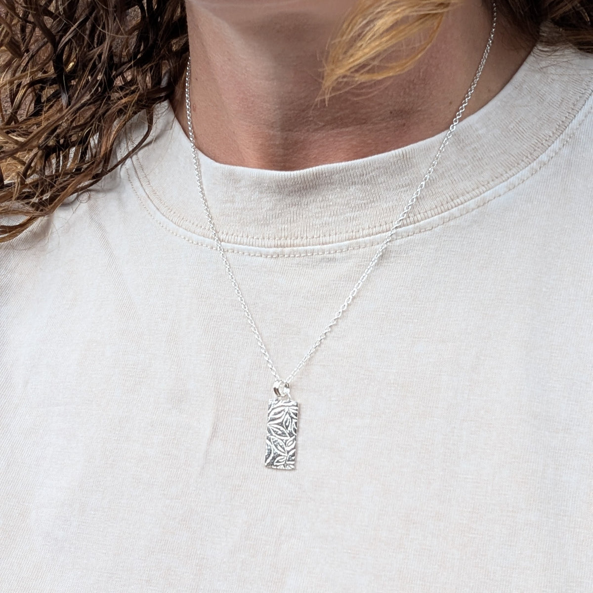 Silver leaves rectangle necklace handmade from recycled Sterling Silver, shown being worn with the textured rectangular pendant hanging from a silver chain.
