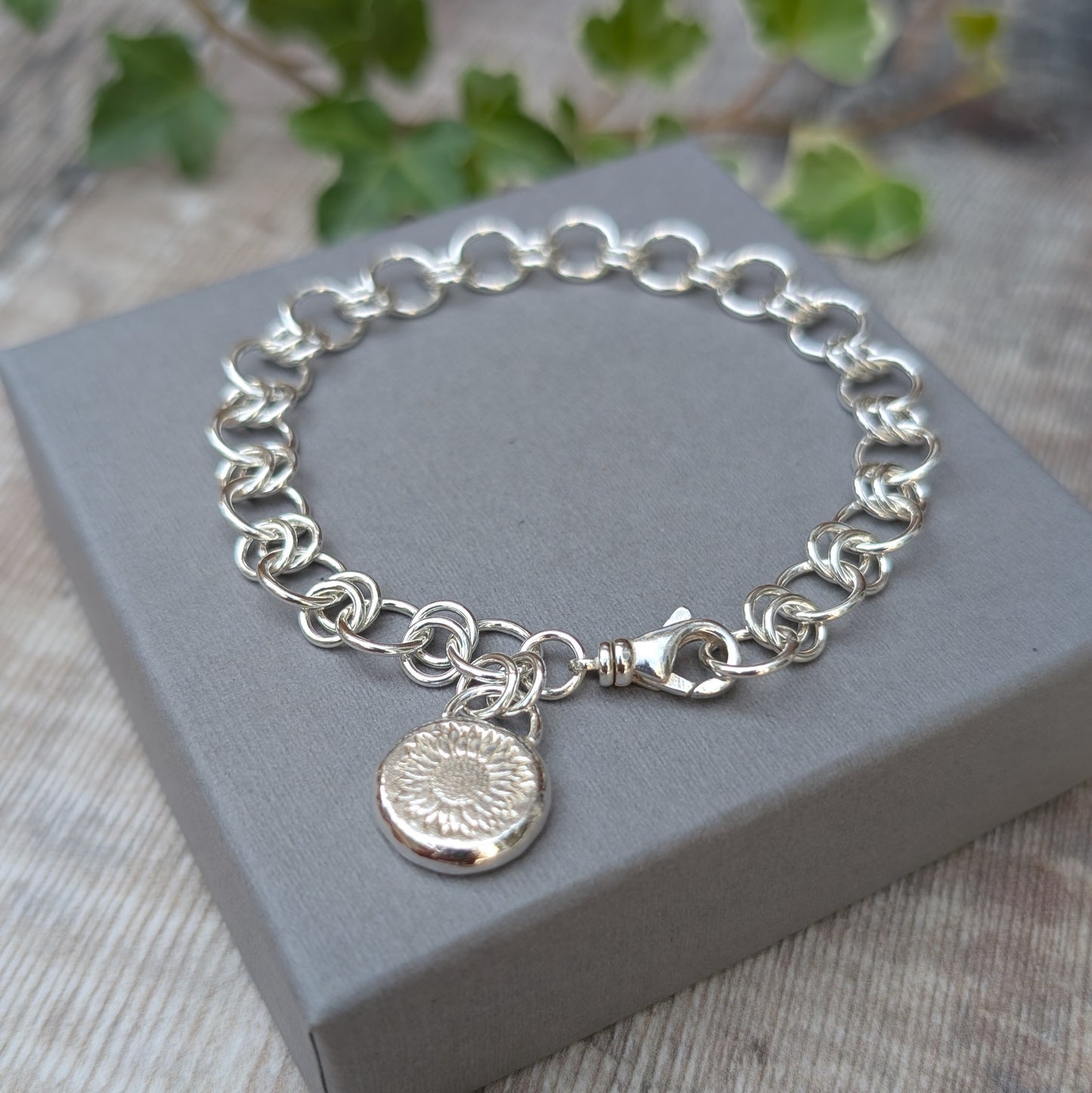 Silver Chain Link Bracelet with Sunflower Charm displayed on a grey jewellery box, showing the hand forged and soldered Sterling Silver chain links with the handmade sunflower pebble charm.