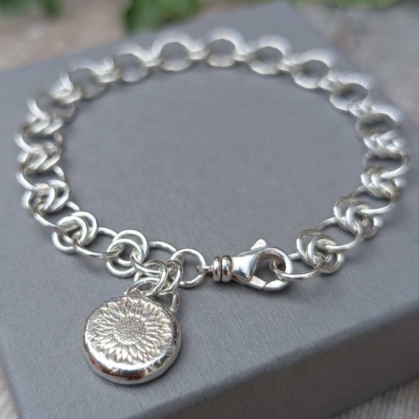 Silver Chain Link Bracelet with Sunflower Charm made from recycled Sterling Silver, shown on a grey jewellery box with handmade chain links and a round sunflower pebble charm.
