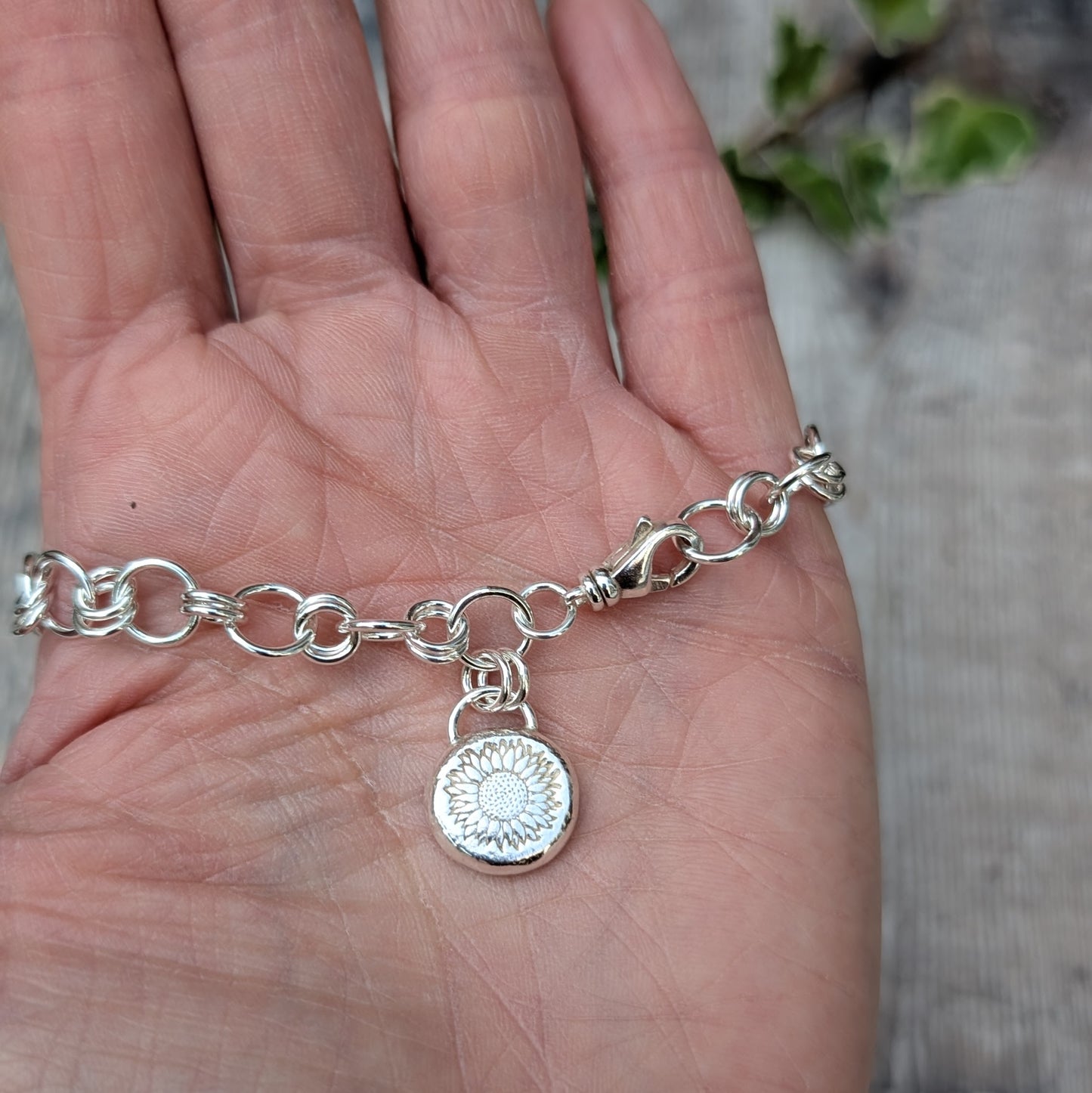 Silver Chain Link Bracelet with Sunflower Charm held in the palm of a hand, showing the handmade chain links, lobster clasp and stamped sunflower silver pebble charm.