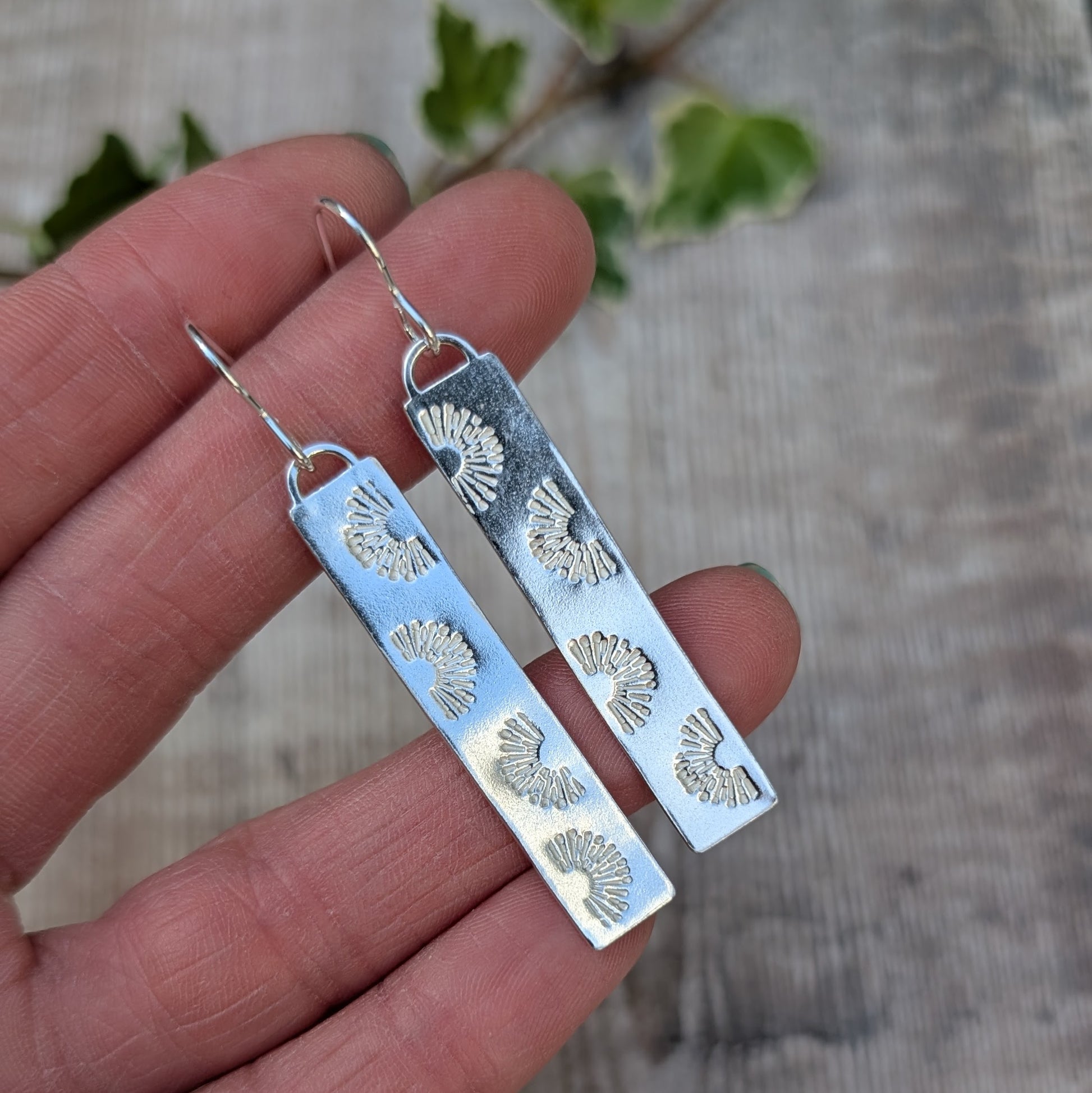 Silver long rectangle sunrise earrings handmade from recycled Sterling Silver, held in a hand to show the long shape and hand stamped sunrise pattern.