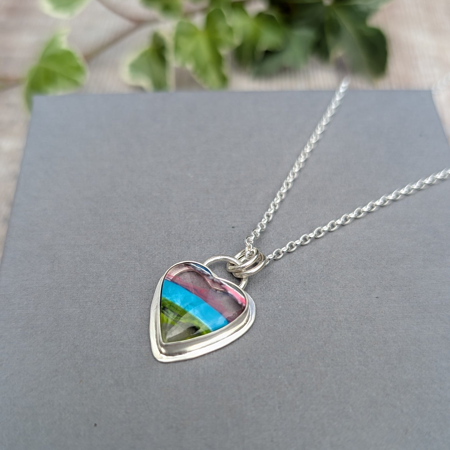 Close up of Silver Multicoloured Surfite Heart Necklace on a grey background with colourful layered Surfite set in recycled Sterling Silver.