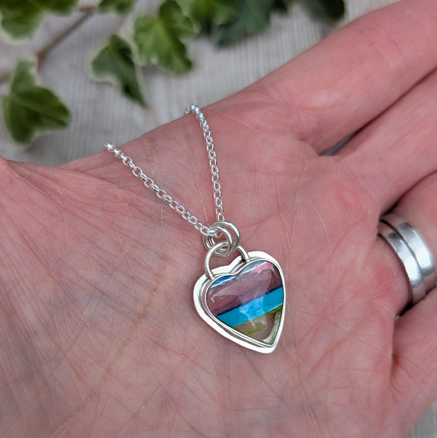 Silver Multicoloured Surfite Heart Necklace held in a hand, showing the handmade silver setting and colourful layered Surfite.