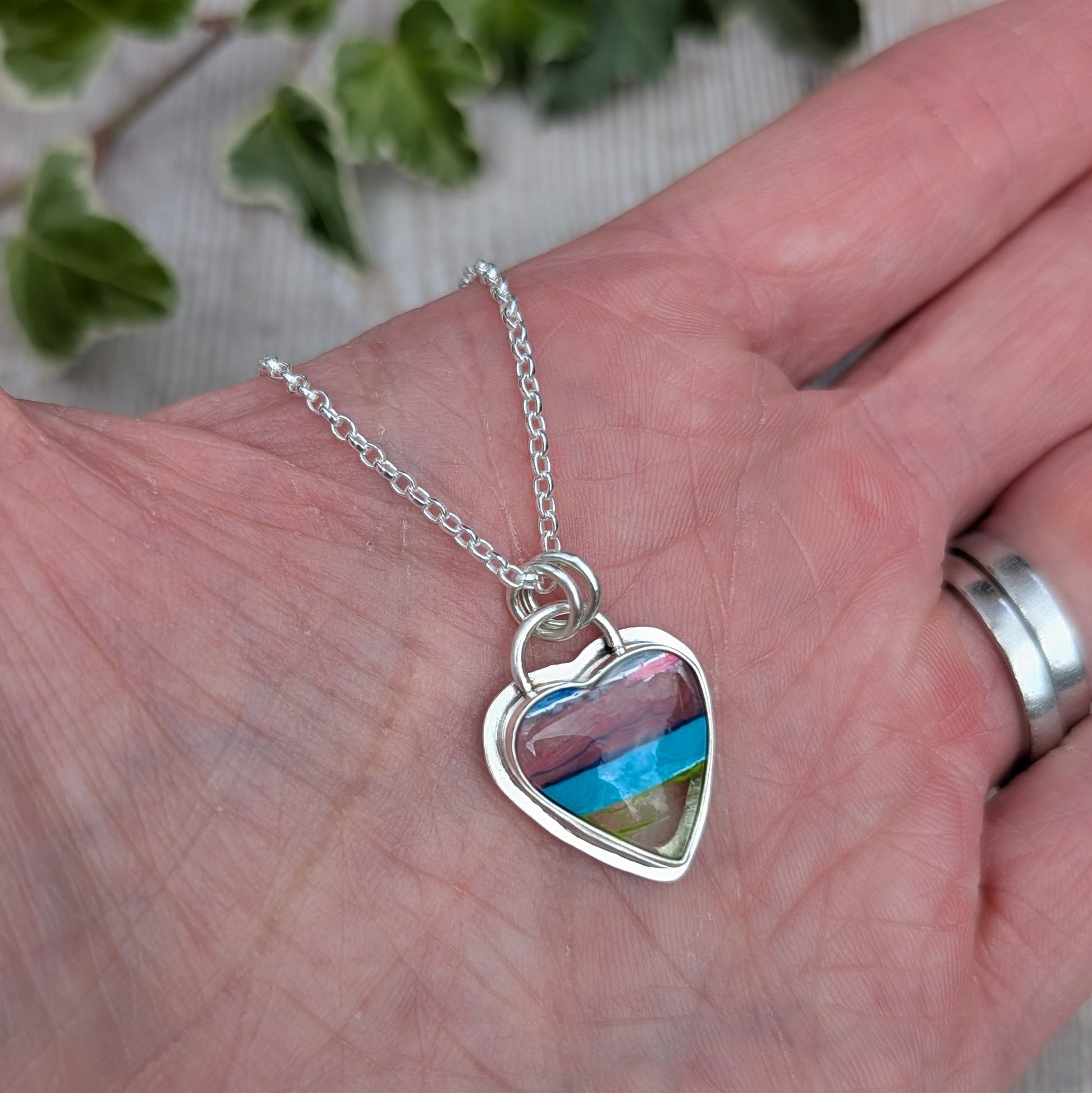 Silver Multicoloured Surfite Heart Necklace held in a hand, showing the handmade silver setting and colourful layered Surfite.