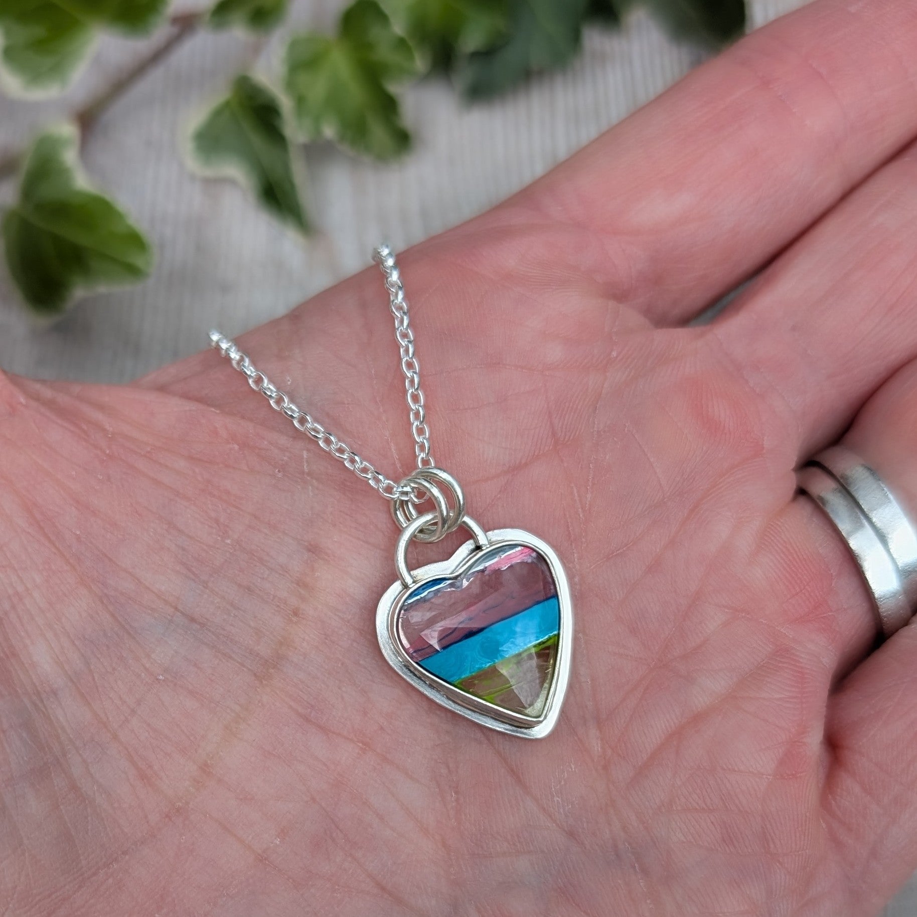 Close up of Silver Multicoloured Surfite Heart Necklace held in a hand, with pink, blue and green layers of Surfite.