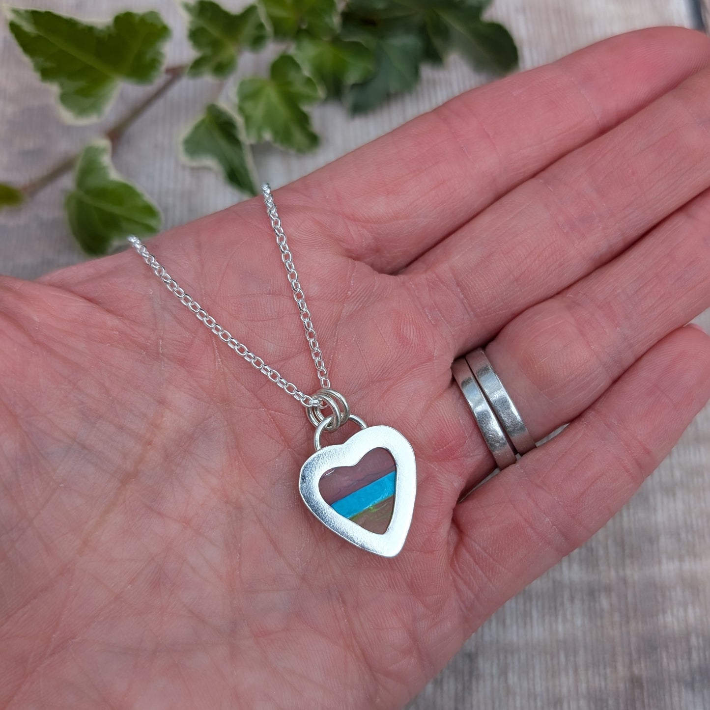 Back of Silver Multicoloured Surfite Heart Necklace held in a hand, showing the open heart shaped silver back.