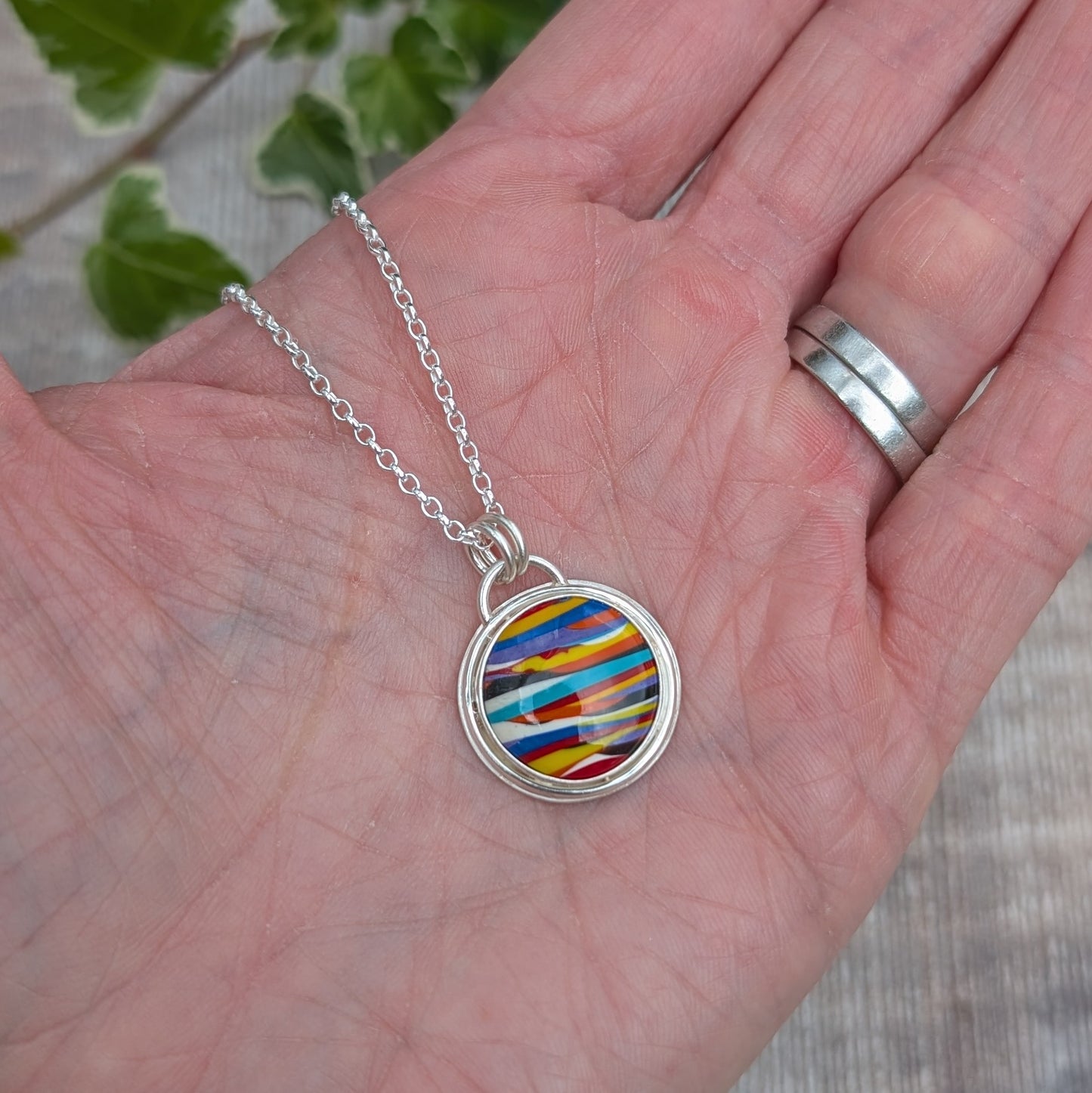 Silver Multicoloured Surfite Round Necklace handmade from recycled Sterling Silver, with a colourful striped round Surfite stone, shown resting on a hand.