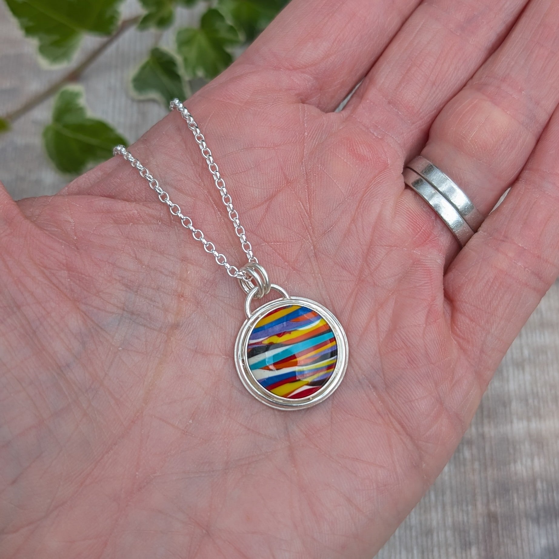 Silver Multicoloured Surfite Round Necklace handmade from recycled Sterling Silver, with a colourful striped round Surfite stone, shown resting on a hand.