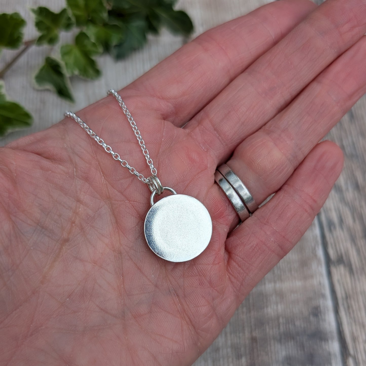 Back view of the Silver Multicoloured Surfite Round Necklace showing the smooth round recycled Sterling Silver setting and silver chain, resting on a hand.