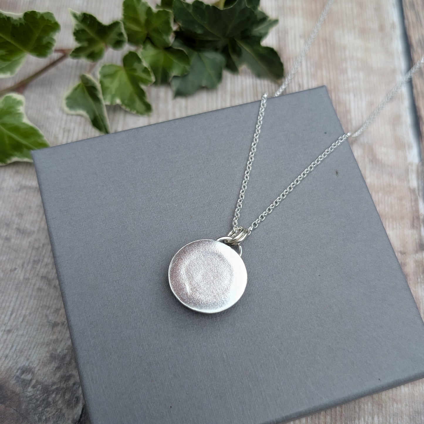Back view of the Silver Multicoloured Surfite Round Necklace showing the handmade round Sterling Silver setting and chain on a grey display box.