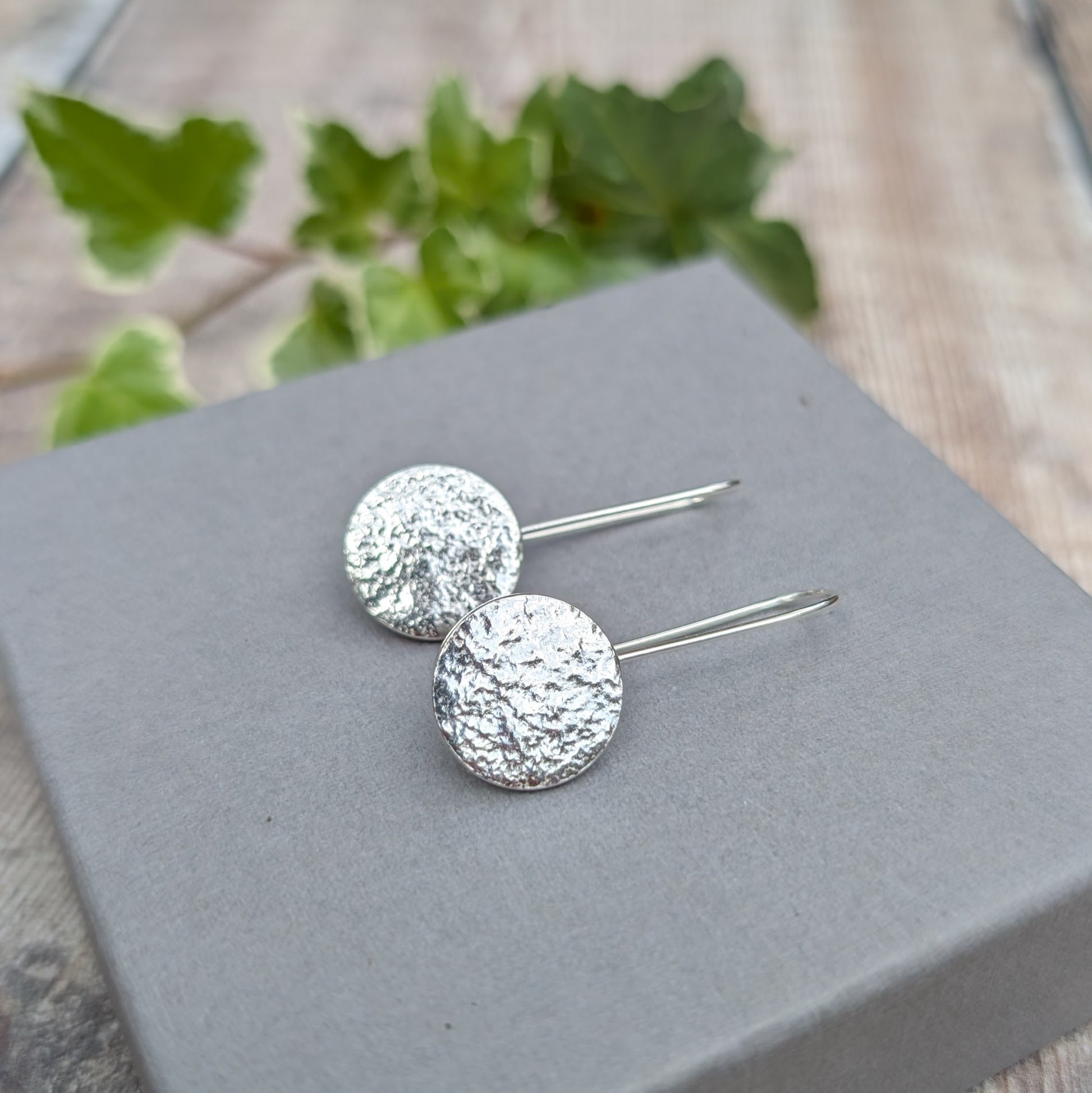 Silver organic disc long earrings handmade from recycled Sterling Silver, with textured circular discs resting on a grey jewellery box.