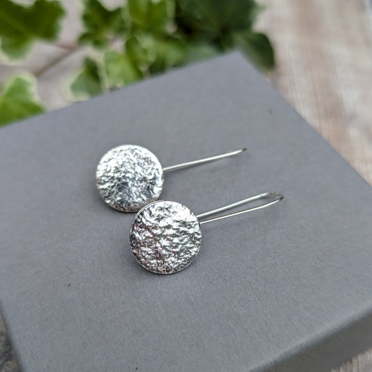 Silver organic disc long earrings handmade from recycled Sterling Silver, with textured round discs and long ear wires, displayed on a grey box.