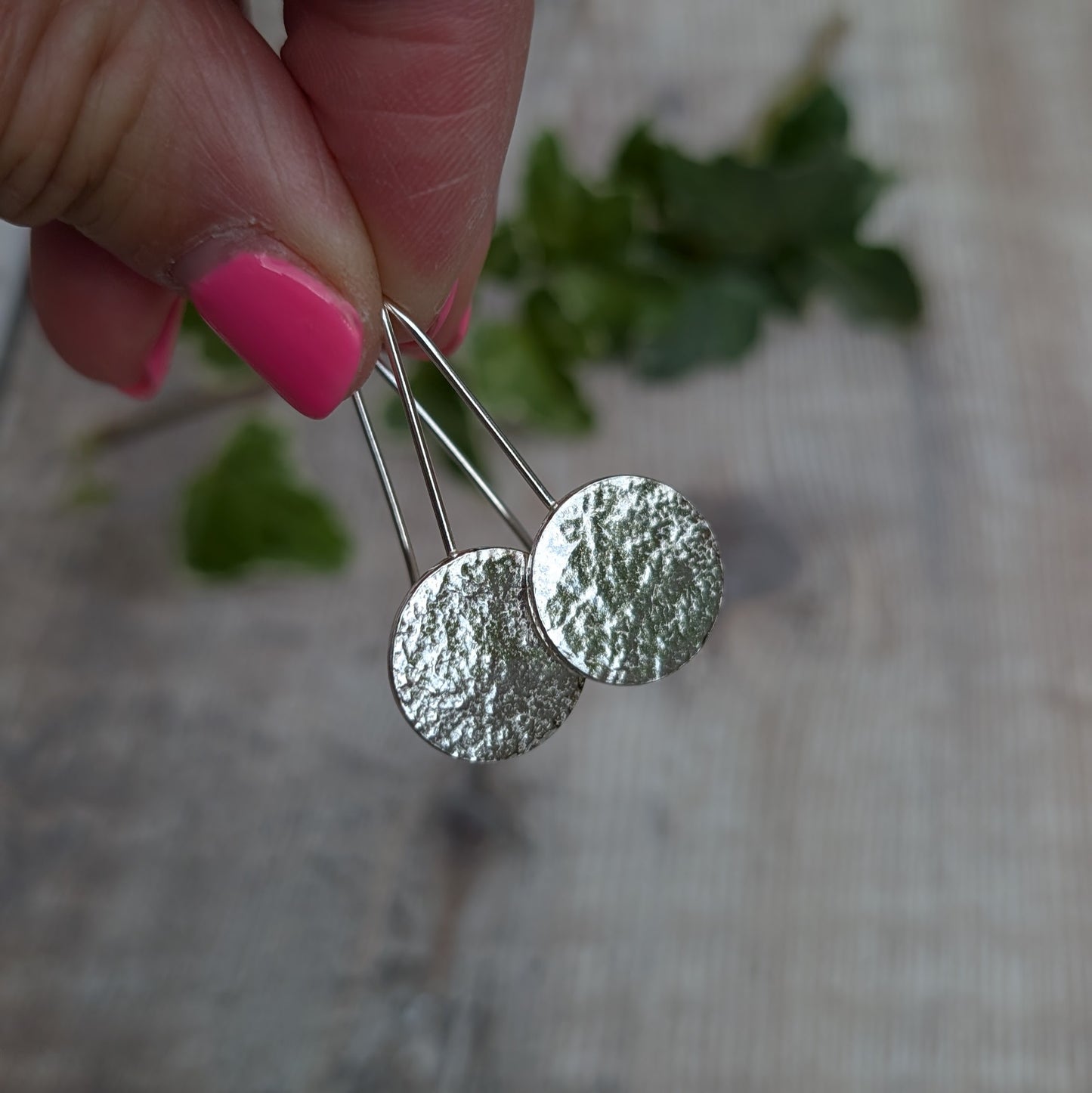 Silver organic disc long earrings held up by their ear wires, showing the uneven organic texture on the recycled Sterling Silver discs.