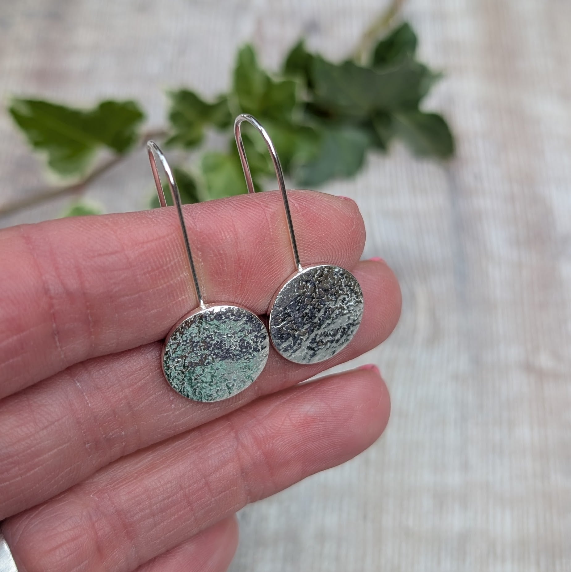 Close up of silver organic disc long earrings held in a hand, showing the textured surface of each round silver disc.