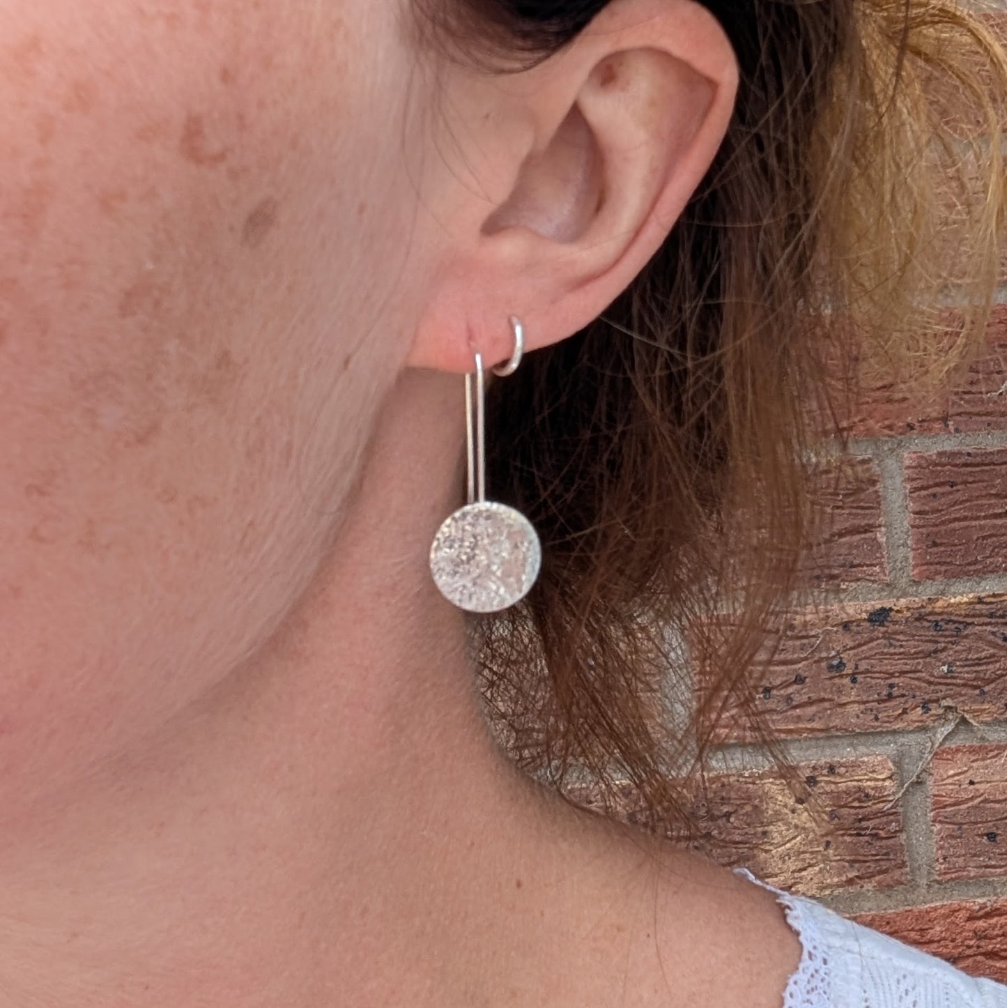 Silver organic disc long earrings being worn, showing the length and size of the textured round disc design.