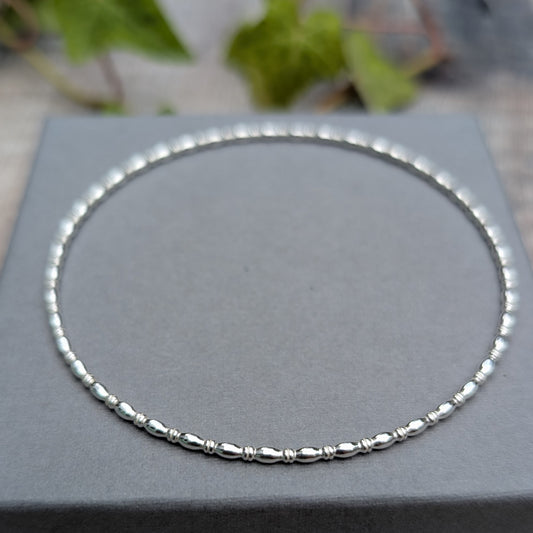 Silver Oval Beaded Wire Round Bangle handmade from recycled Sterling Silver 2mm square wire, shown flat on a grey jewellery box.