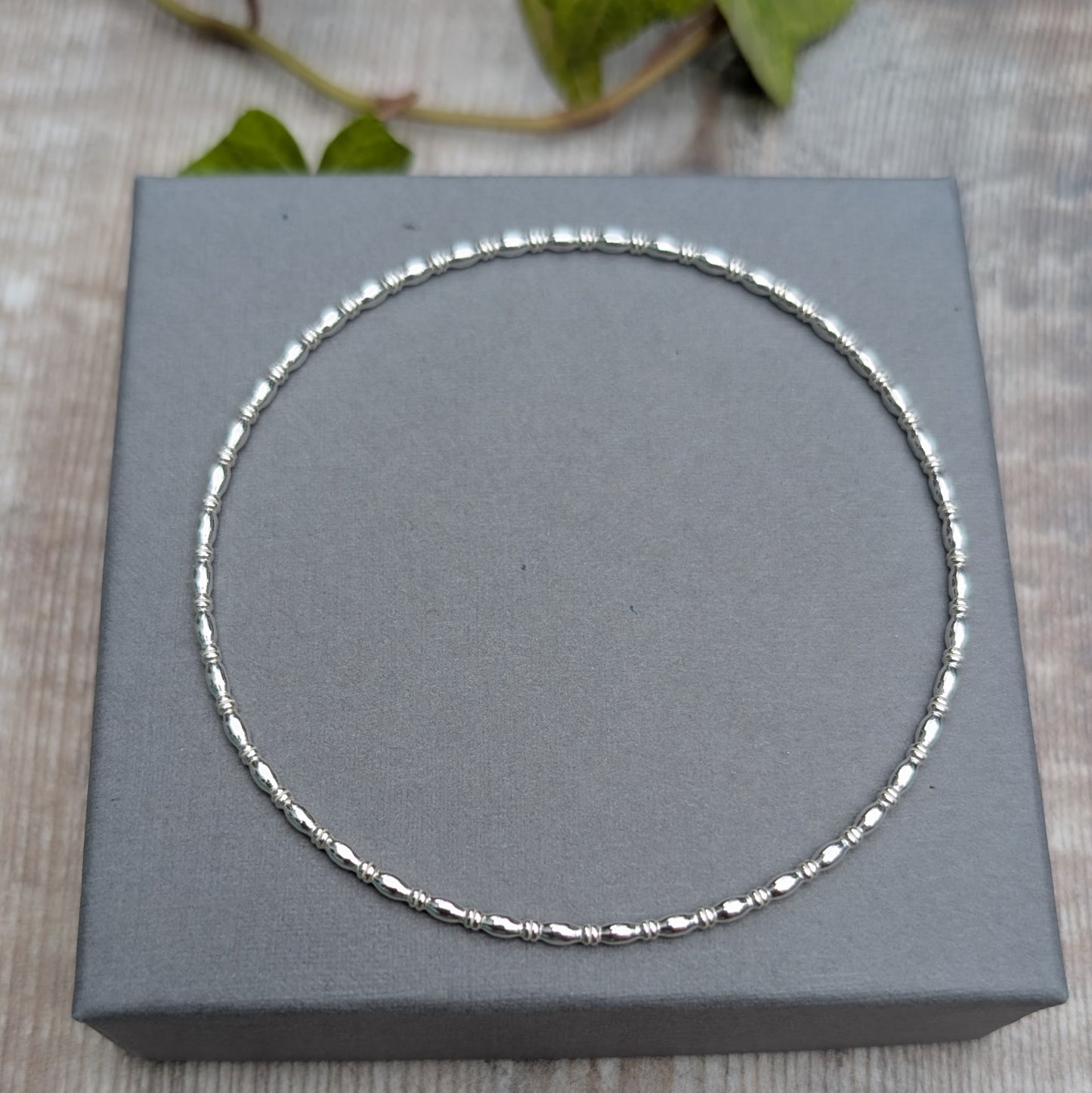 Silver Oval Beaded Wire Round Bangle handmade from recycled Sterling Silver 2mm square wire, photographed from above on a grey jewellery box.