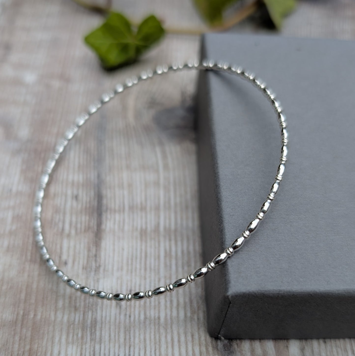 Silver Oval Beaded Wire Round Bangle handmade from recycled Sterling Silver 2mm square wire, shown standing at an angle to highlight the oval beaded pattern.