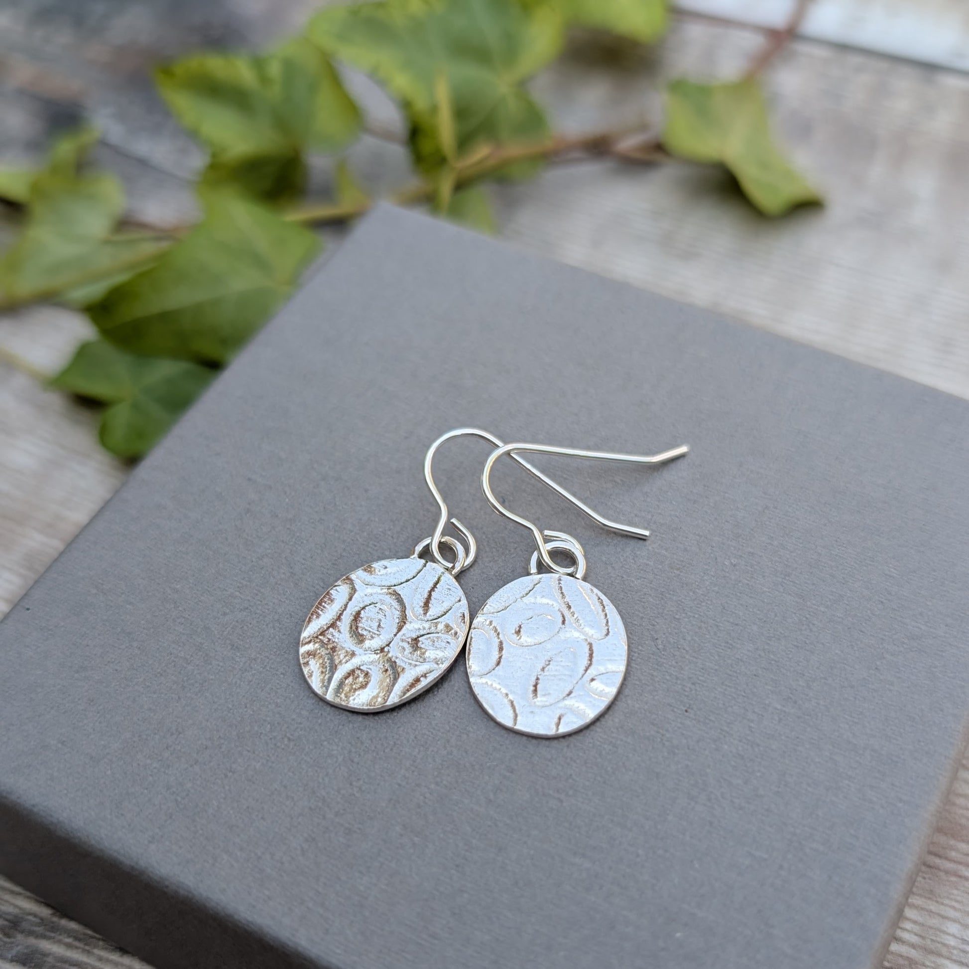 Silver Oval Disc Earrings with Oval Pattern shown close up on a grey box outdoors