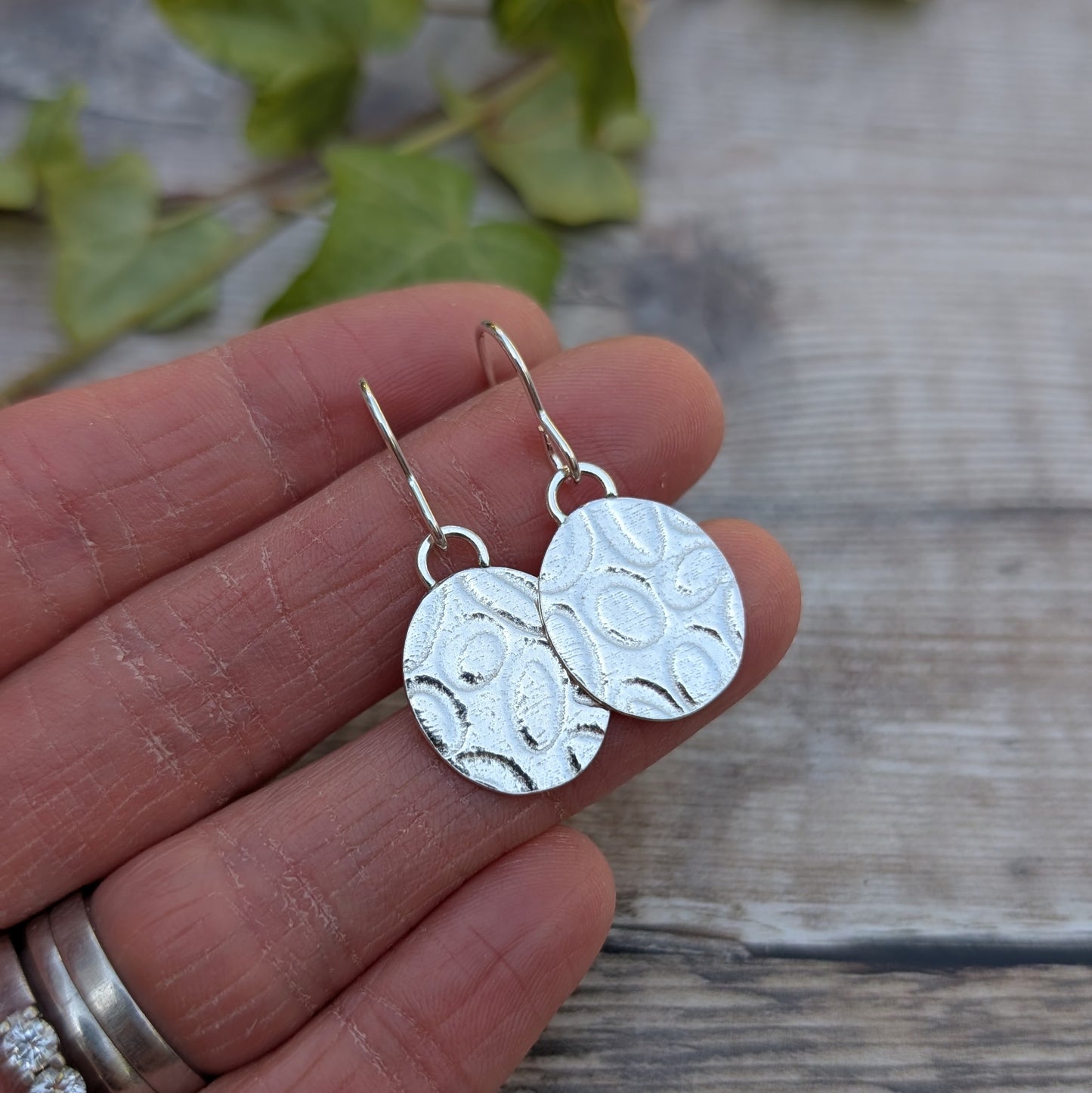 Silver Oval Disc Earrings with Oval Pattern held in a hand showing size and detail