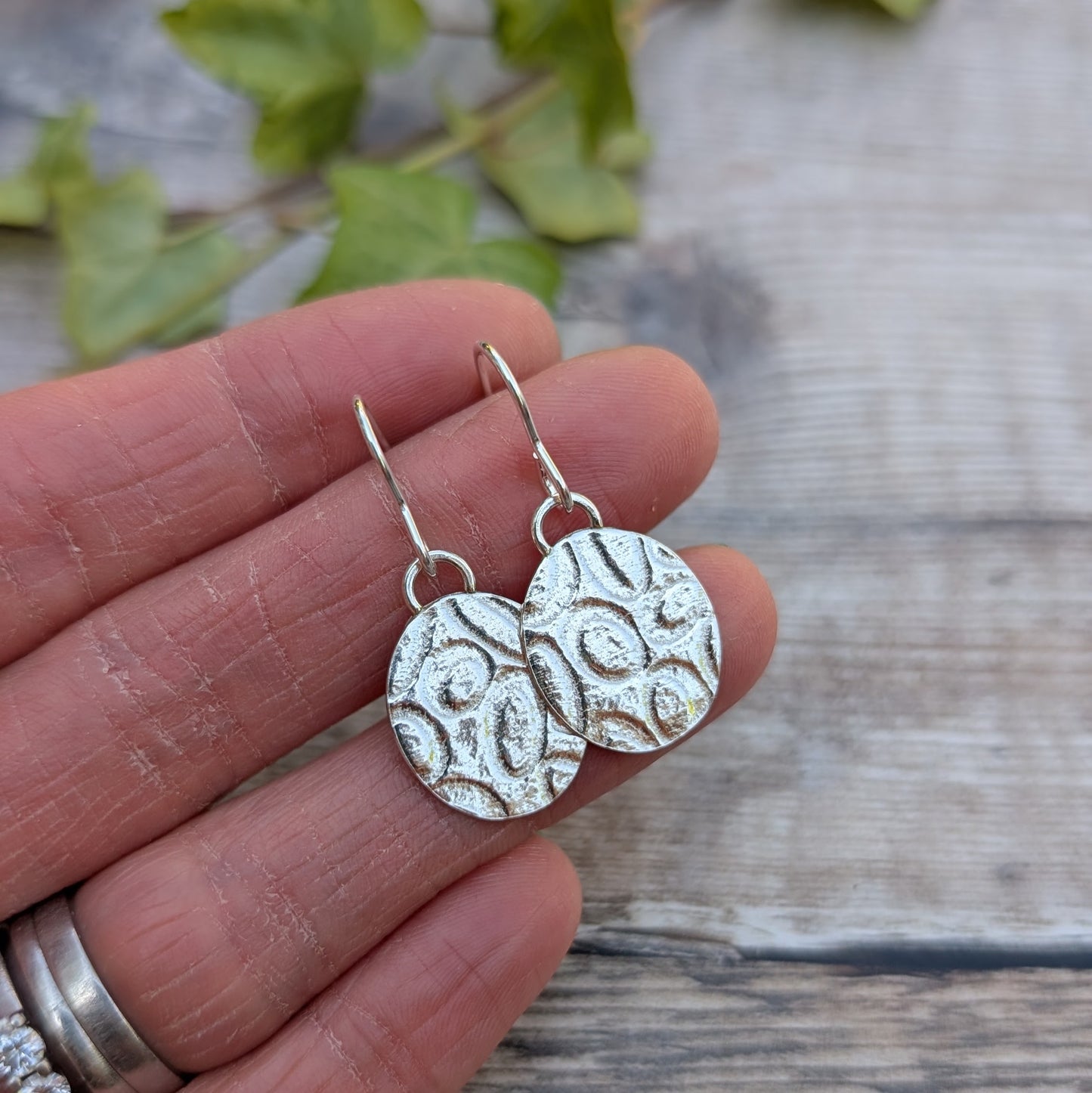 Silver Oval Disc Earrings with Oval Pattern close up in hand showing pressed oval texture