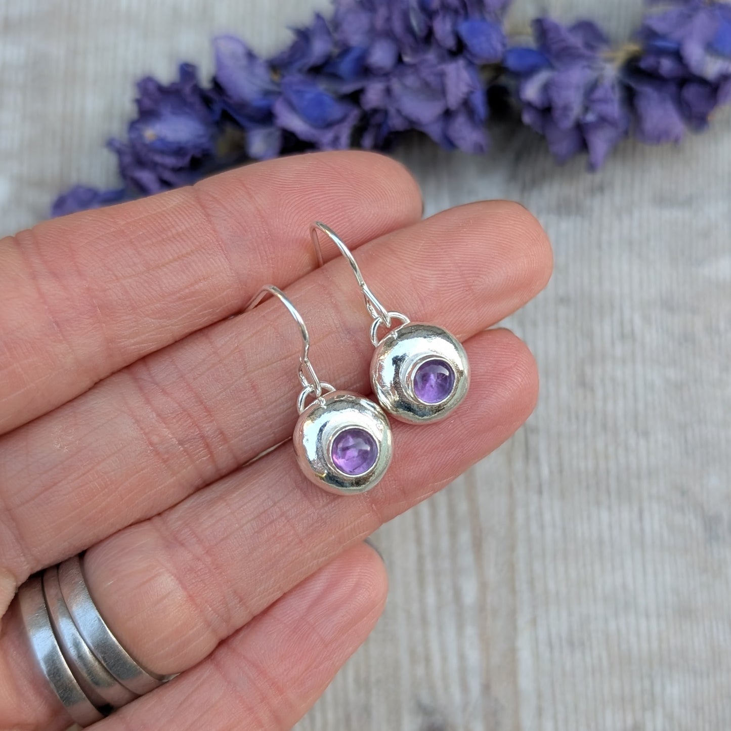 Hand holding silver pebble earrings with Amethyst to show their size and detail.