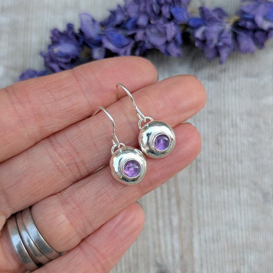 Hand holding silver pebble earrings with Amethyst to show their size and detail.