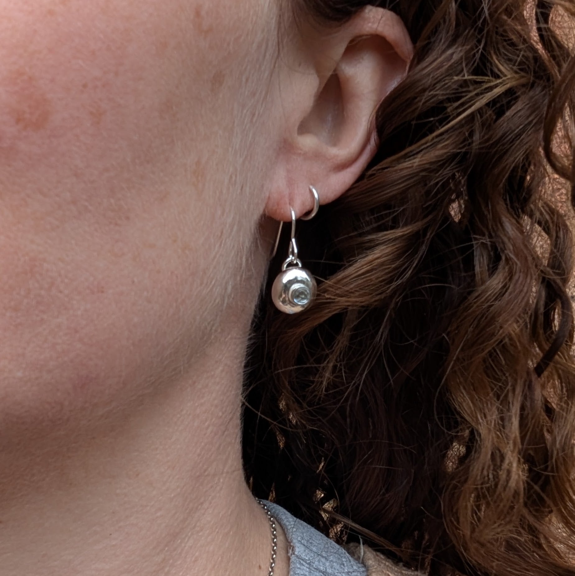 Silver pebble earrings with Aquamarine worn on the ear.
