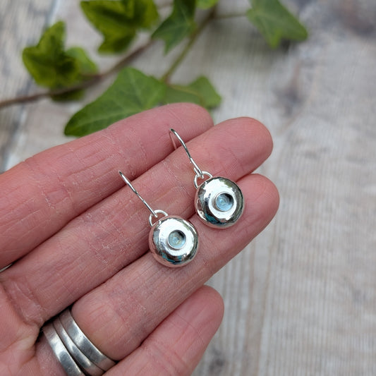 Silver Pebble Earrings with Blue Topaz held in hand showing small round silver discs with blue stones