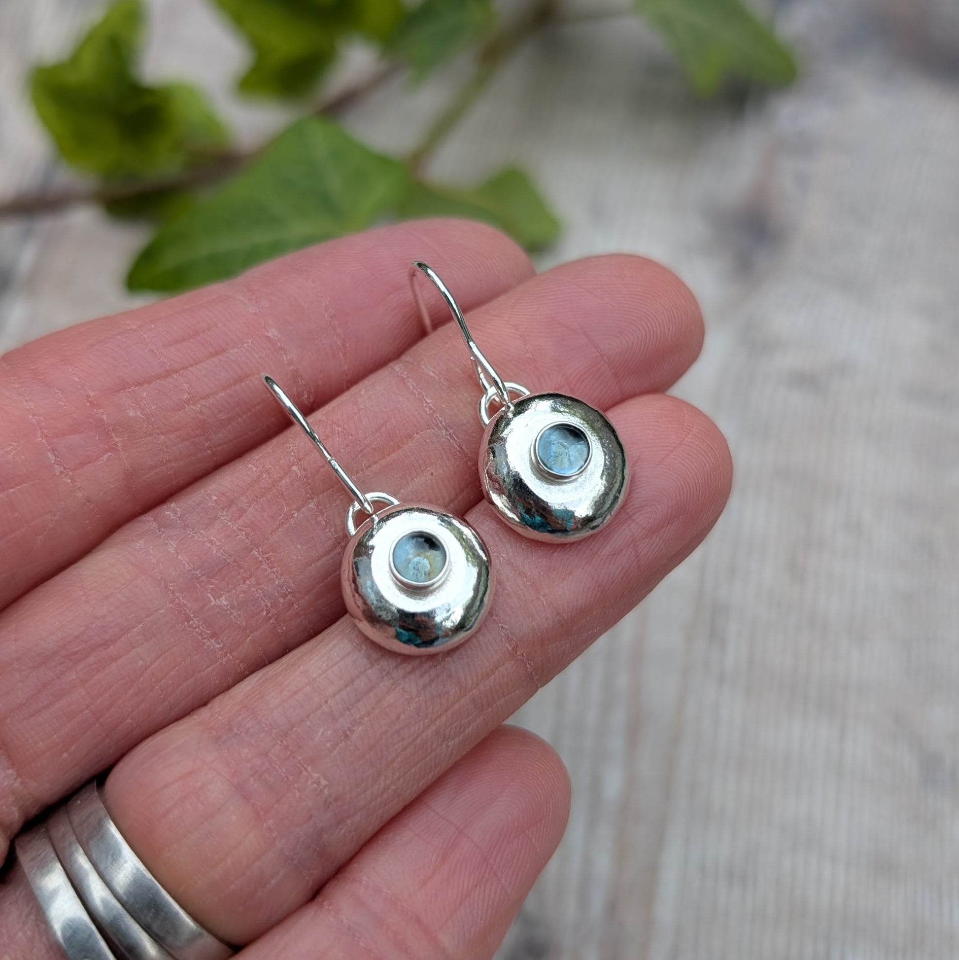 Close up of Silver Pebble Earrings with Blue Topaz in hand showing handmade silver detail