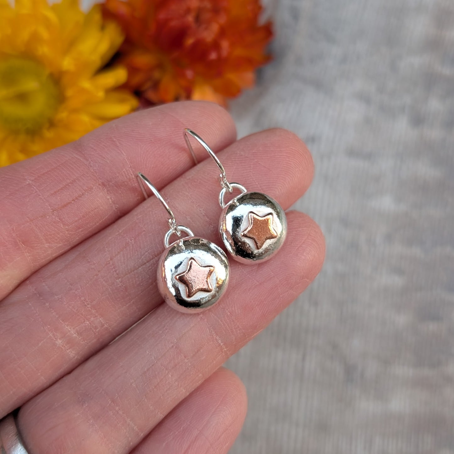 Silver pebble earrings with copper star motifs, photographed in the hand to show size and shine.