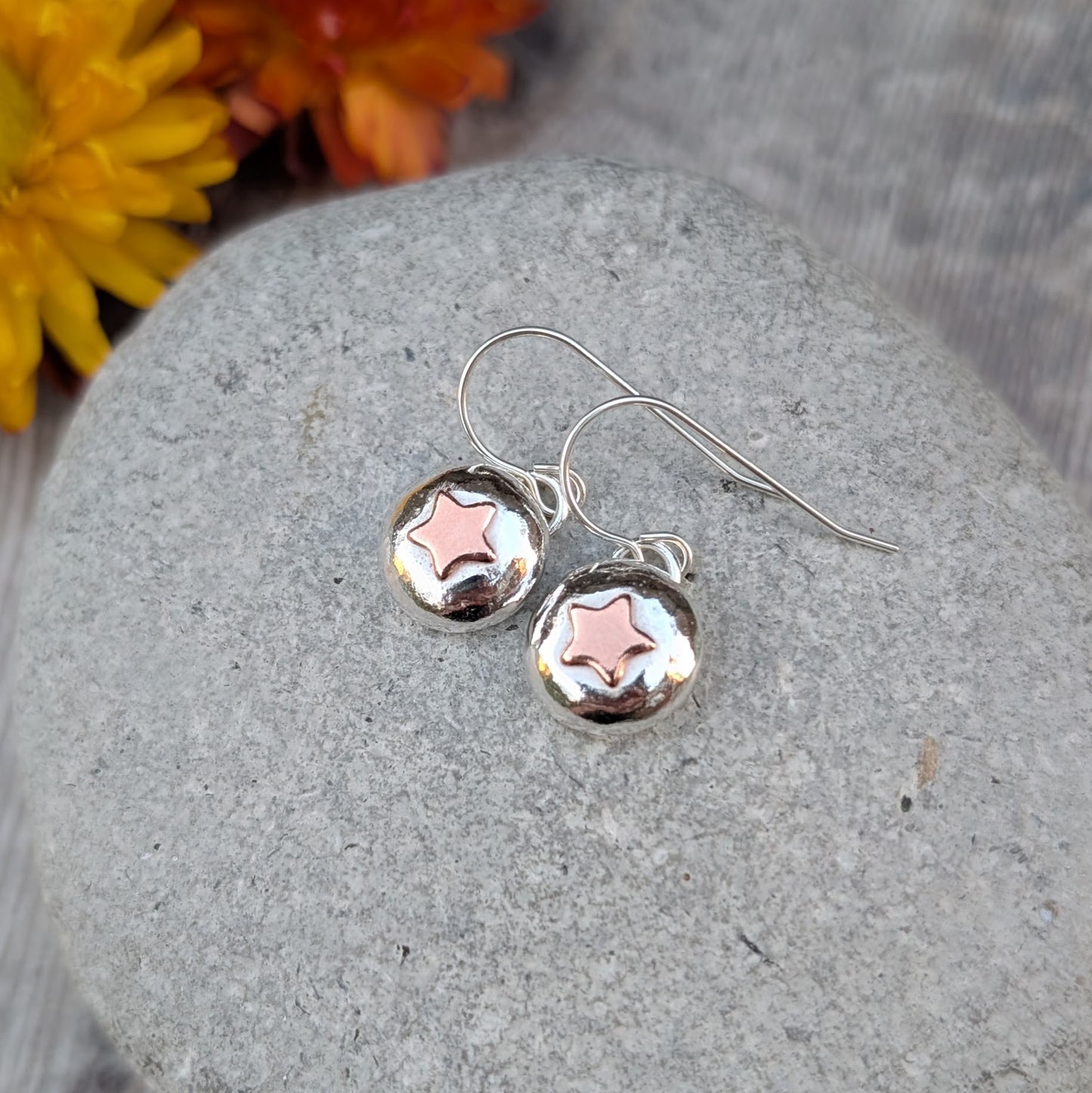 Sterling silver drop earrings featuring rounded pebble shapes with copper stars, displayed on a stone.