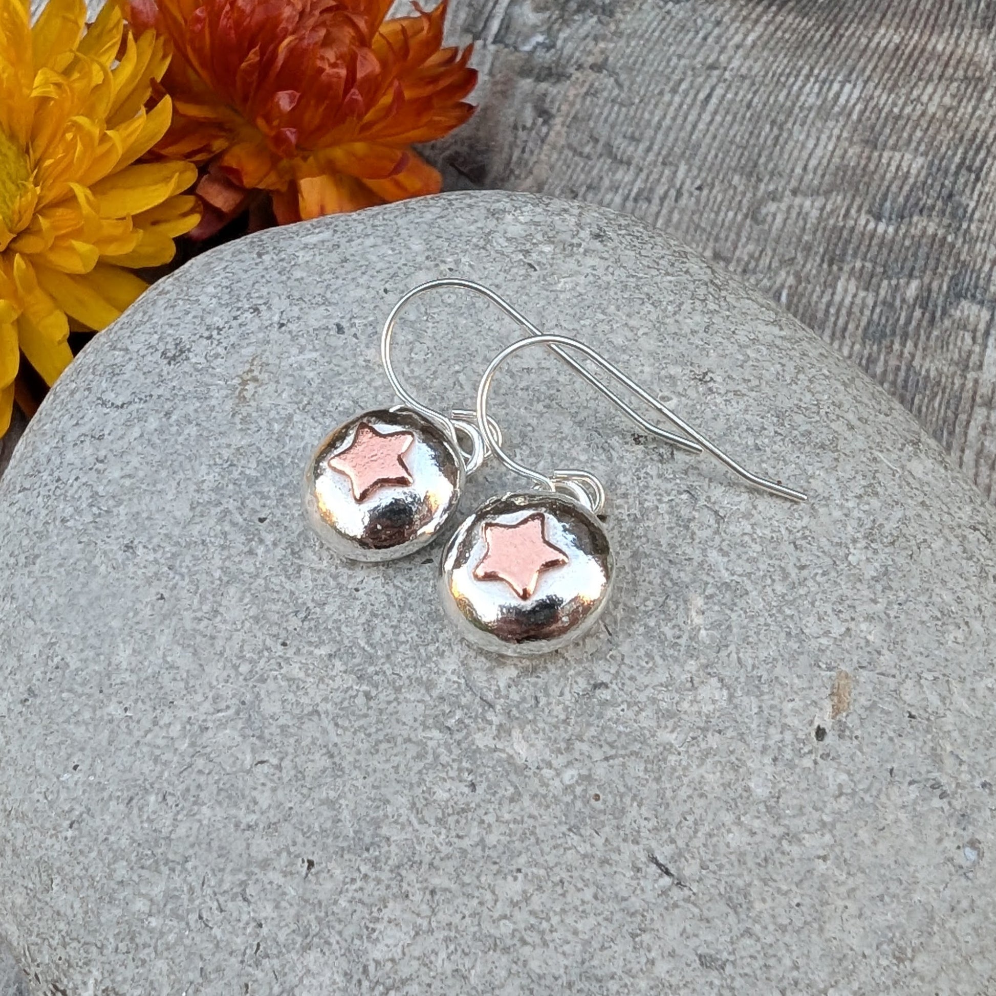 Close-up of silver pebble earrings with copper star details and sterling silver hooks.