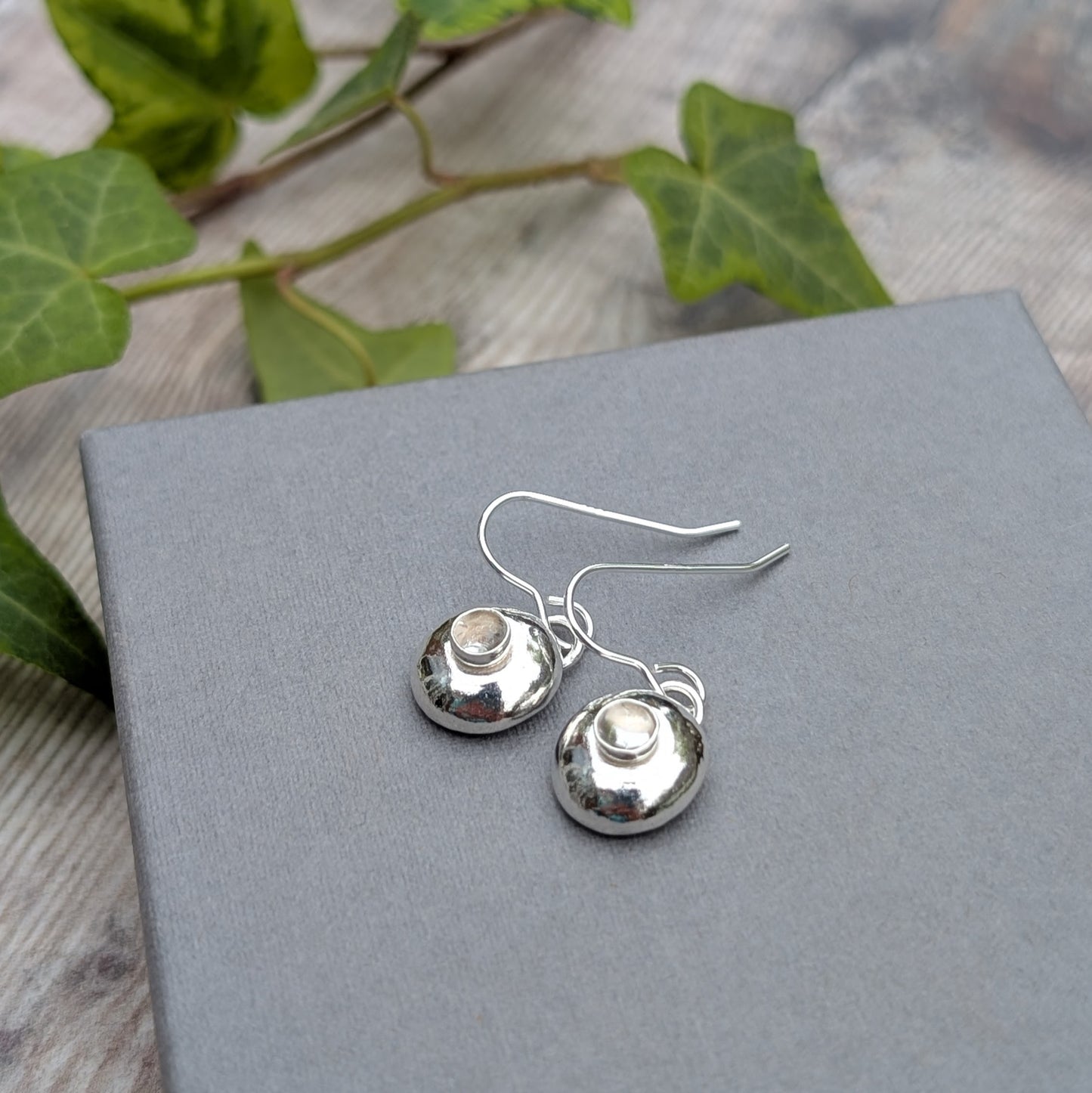 Silver Pebble Earrings with Crystal Quartz displayed on a grey box with natural background