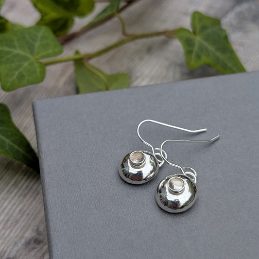 Silver Pebble Earrings with Crystal Quartz resting on a grey box with green leaves in the background