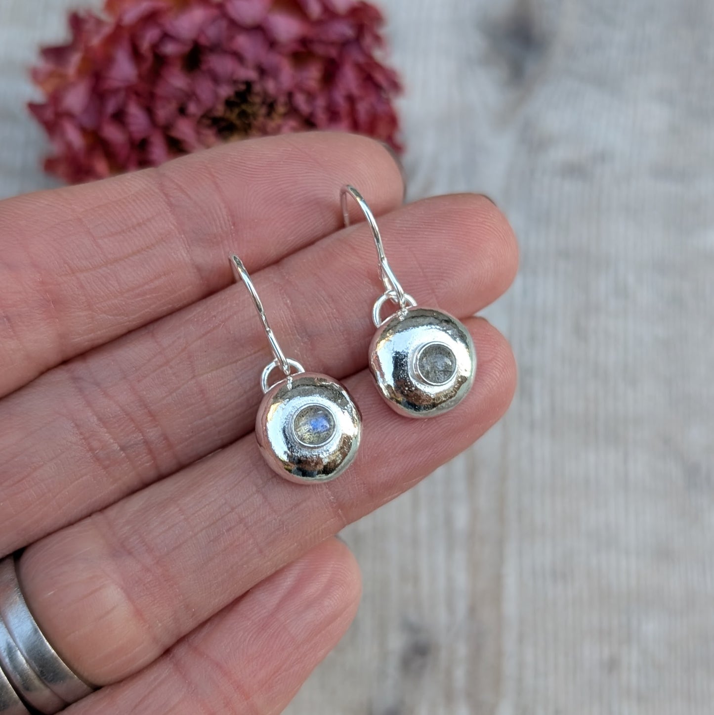 Hand holding silver pebble earrings with Labradorite to show their size and detail.