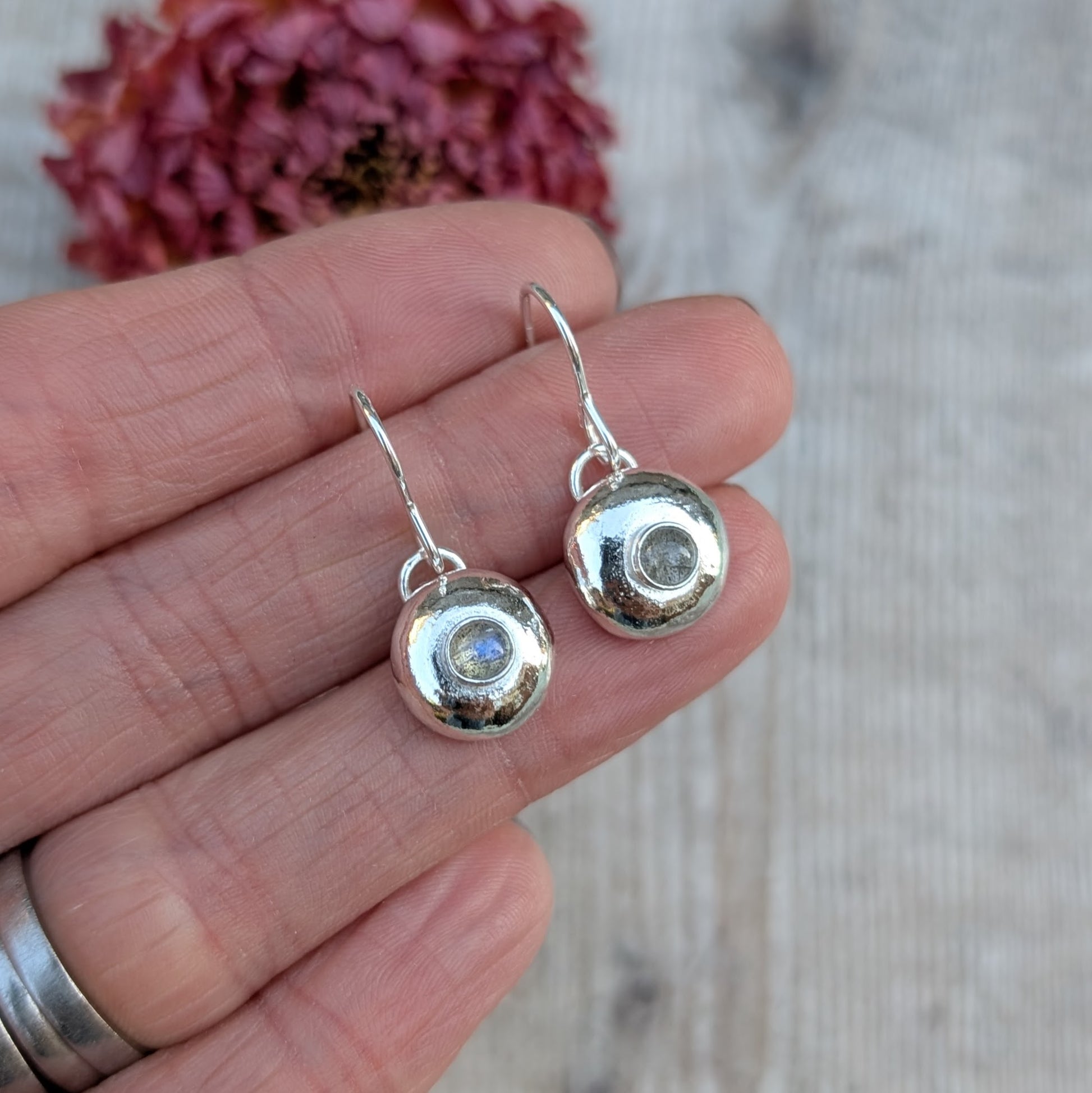 Hand holding silver pebble earrings with Labradorite to show their size and detail.