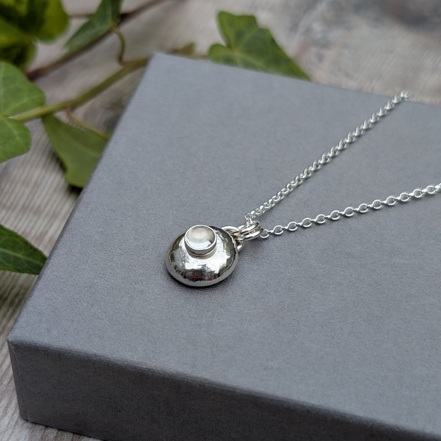 Silver Pebble Necklace with Crystal Quartz on a grey box with ivy leaves and wooden background