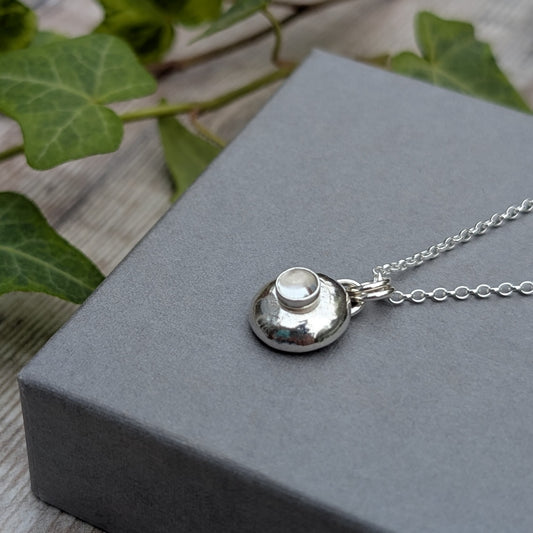 Silver Pebble Necklace with Crystal Quartz resting on a grey box with green ivy in the background