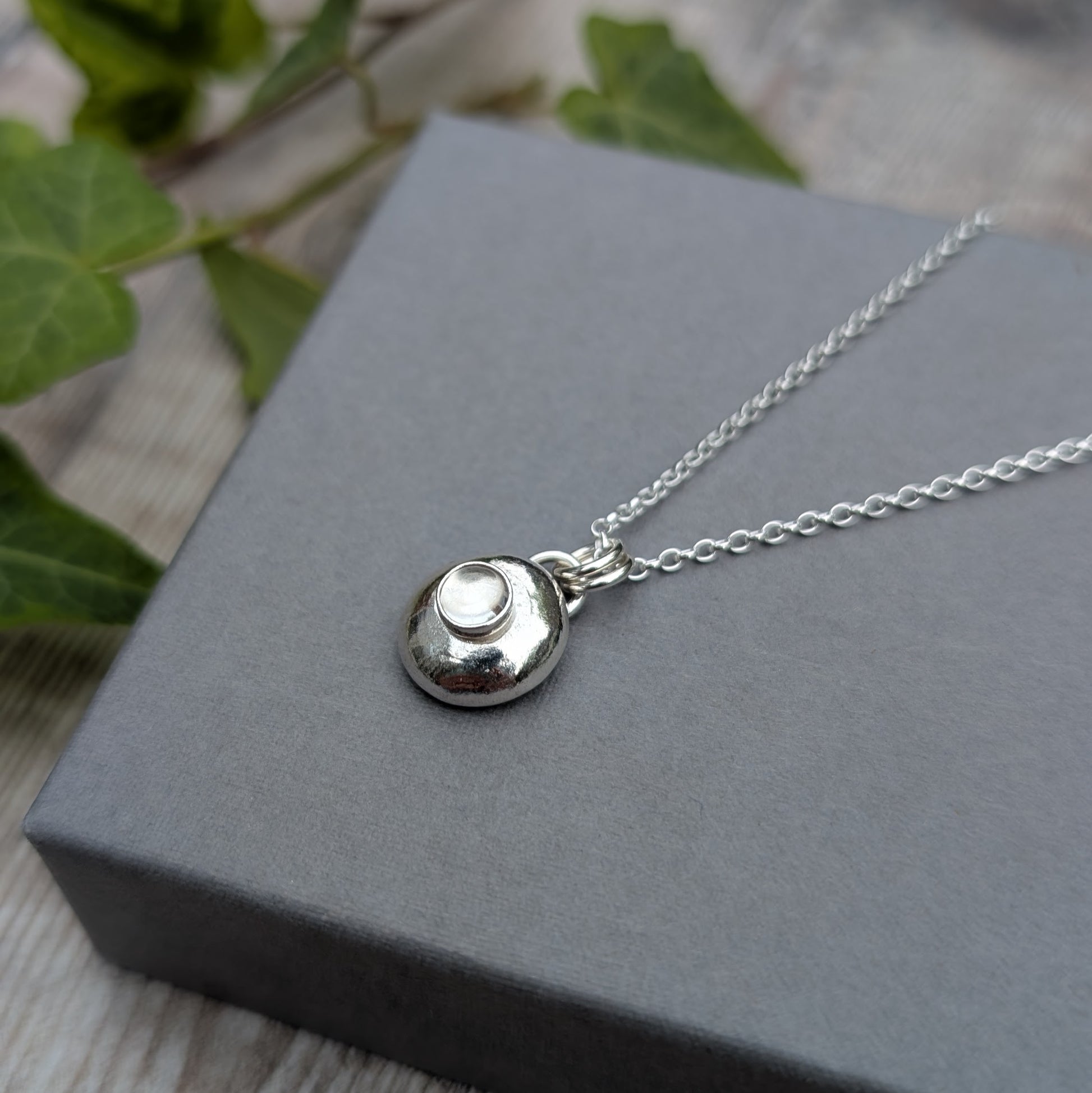 Silver Pebble Necklace with Crystal Quartz on a grey box showing chain detail and polished finish