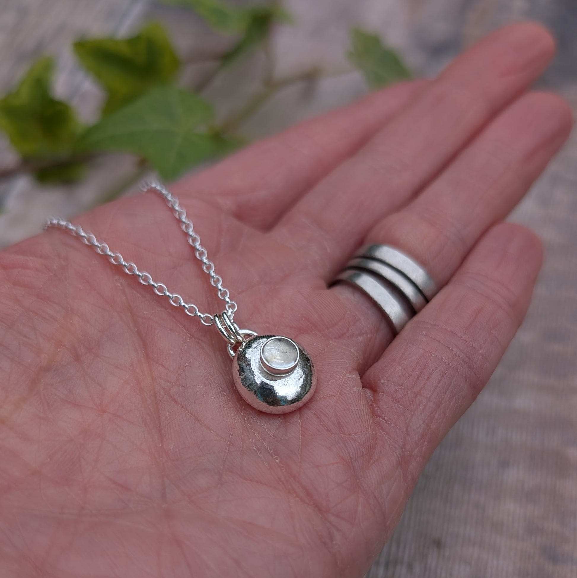 Silver Pebble Necklace with Crystal Quartz in a hand with rings, showing close up detail of the stone