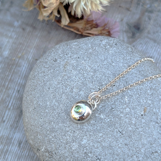 Close-up of silver pebble necklace with Peridot displayed on a grey stone.