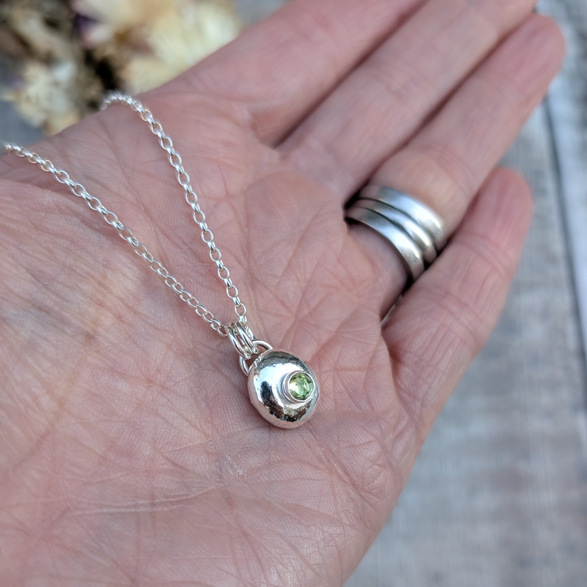 Hand holding silver pebble necklace with Peridot to show the pendant size and detail.
